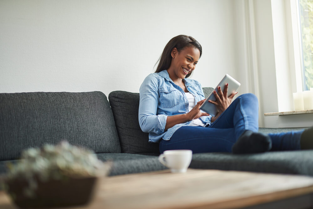 Imagem de uma mulher negra sentada em um sofá. Ela está lendo um livro.