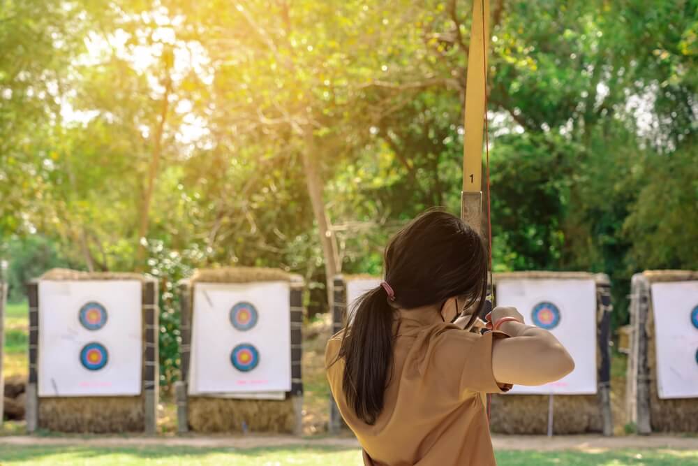Imagem de uma menina mirando em um alvo com uma flecha.