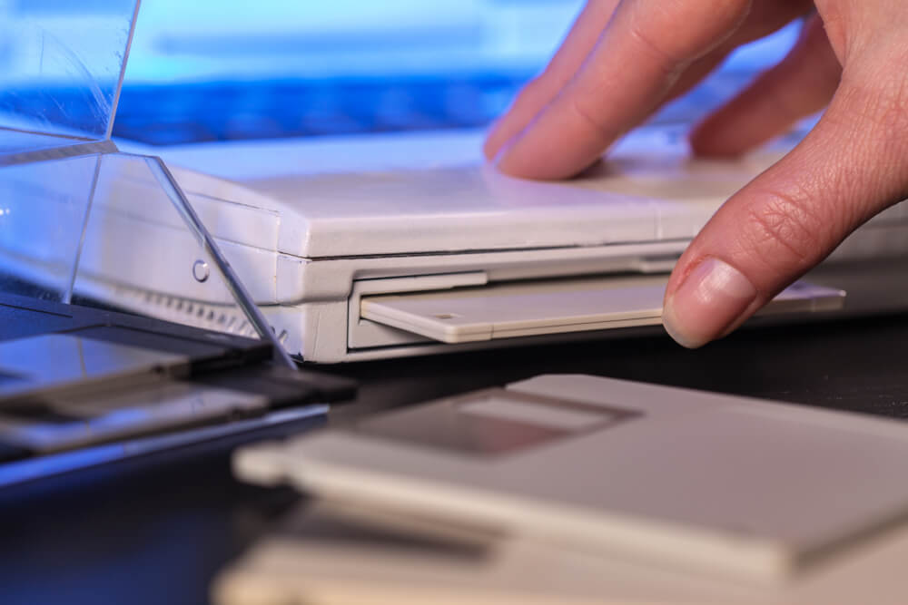 Imagem de uma mão branca inserindo um disquete em um computador.