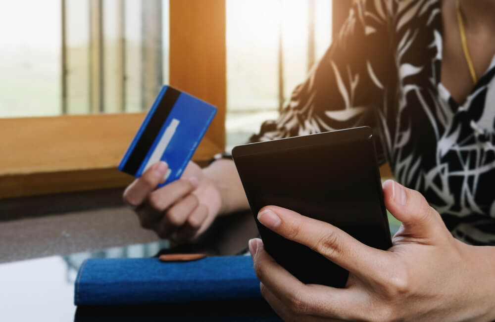 Imagem de uma mulher segurando o celular em uma das mãos e, na outra, o cartão de crédito, pronta para fazer compras na Cyber Monday 2023.